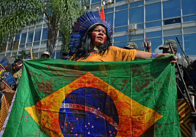 (FILES) In this file photo taken on April 26, 2019, an indigenous woman holds a Brazilian national flags stained in red -as blood- during a march in Brasilia on the last day of a protest to defend indigenous land and rights. Brazilian indigenous leader Ailton Krenak said that President Jair Bolsonaro must be "internationally condemned" for his offensive against indigenous reserves, which he intends to open to mining and agriculture. / AFP / CARL DE SOUZA
