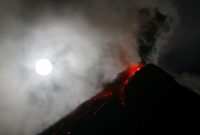 The super blue blood moon sets before dawn as lava cascades down the slopes of Mayon volcano during its sporadic mild eruption as seen from Sto. Domingo township, Albay province around 340 kilometers (200 miles) southeast of Manila, Philippines Thursday, Feb. 1, 2018. It's the first time in 35 years a blue moon has synced up with a supermoon and a total lunar eclipse, or blood moon because of its red hue. (AP Photo/Bullit Marquez)