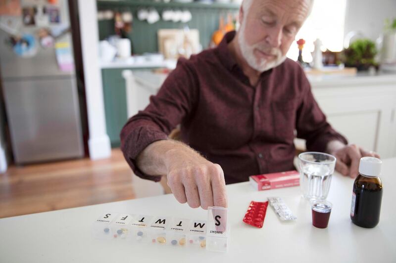 Senior man organizing pill box at kitchen table. Getty Images
