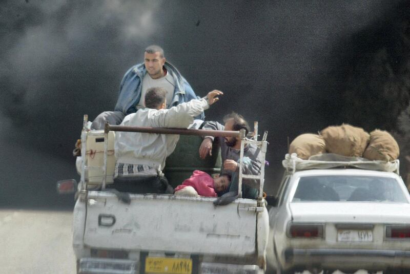 Iraqis fleeing Baghdad sit with their belongings in the back of a pick-up truck 31 March 2003, as smoke billowing from burning oil trenches covers the sky. Coalition warplanes pounded the Iraqi capital and its outskirts, with loud explosions rocking the city.    AFP PHOTO/Ramzi HAIDAR (Photo by RAMZI HAIDAR / AFP)