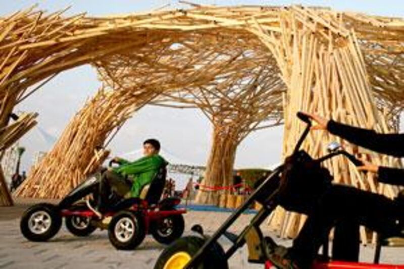 Two boys ride past a domed wooden sculpture comprising seven pillars at the Corniche in Abu Dhabi yesterday.