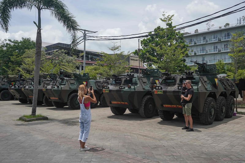 Tourists pose for pictures in front of police-armoured vehicles parked near the venue of the G20 Bali Summit in Nusa Dua, Bali.  AFP