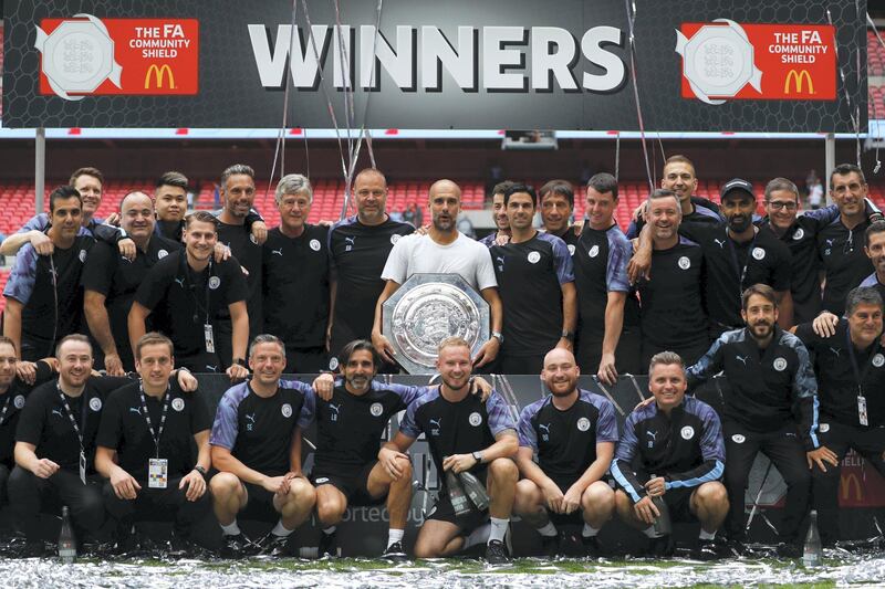 Manchester City's Spanish manager Pep Guardiola holds the trophy as he poses with his staff after winning the English FA Community Shield football match between Manchester City and Liverpool at Wembley Stadium in north London on August 4, 2019. (Photo by Adrian DENNIS / AFP) / NOT FOR MARKETING OR ADVERTISING USE / RESTRICTED TO EDITORIAL USE