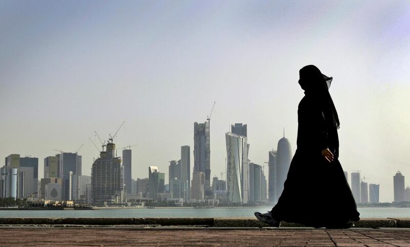 FILE- In this May 14, 2010 file photo, a Qatari woman walks in front of the city skyline in Doha, Qatar. The U.S. military says it has halted some military exercises with Gulf countries over the ongoing diplomatic dispute targeting Qatar. (AP Photo/Kamran Jebreili, File)