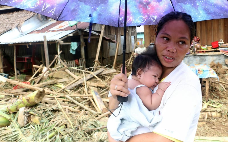 A woman stands with her infant child in front of homes damaged in eastern Samar, Philippines. Rescuers used bulldozers to dig through mountains of mud in the search for more than 40 people missing in the eastern Philippines after landslides triggered by a powerful storm which killed at least 31 at the weekend. Alren Bernonio / AFP Photo
