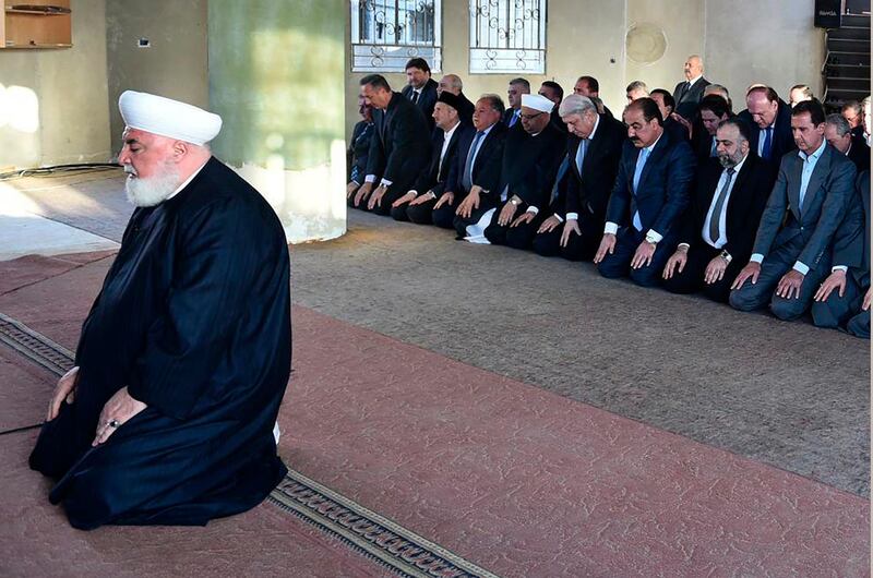 In this photo released on September 12, 2016 by the Syrian official news agency SANA, Syrian President Bashar Assad, right background, prays during Eid al Adha prayers behind Damascus Mufti Mohammed Adnan Afiouni, foreground, in Daraya town suburb of Damascus, Syria. Afiouni who played a key role in government deals with rebel fighters, was killed on Thursday Oct. 22, 2020 by an explosion in the town of Qudsaya, west of Damascus, Syria, when a roadside bomb exploded near him, according to state media and a government site. (SANA via AP)