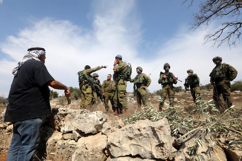 Israeli soldiers stand near a Palestinian farmer waiting to reach a farm to harvest olives in an olive grove on the outskirts of the West Bank village of Yetma, near the Jewish settlement of Rehelim, near Nablus. EPA