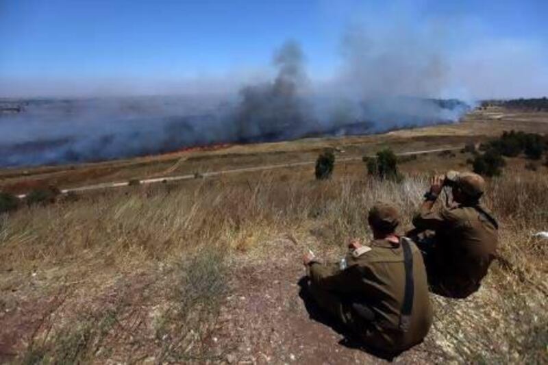 Israeli soldiers north of the Golan Heights watch the Syrian border through smoke, allegedly caused by Syrian mortar shells, after some shells landed on the Israeli side of the border.