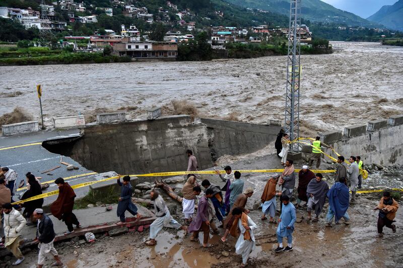 People gather in front of a road damaged by flood waters following heavy monsoon rains in Pakistan's northern Swat Valley. The death toll from devastating monsoon rains is approaching 1,000, with no end in sight. AFP