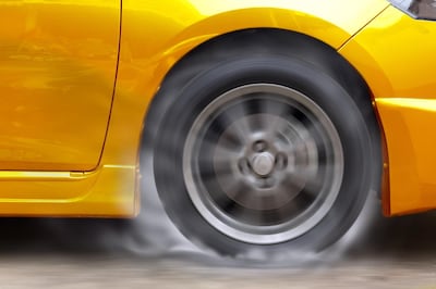 Gold car racing spinning wheel burns rubber on floor.