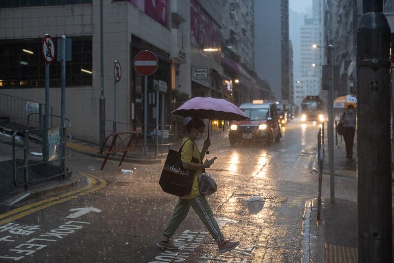 epa09306999 A woman carries an umbrella as she crosses a street during a rain storm in Hong Kong, China, 28 June 2021. The Hong Kong Observatory issued a Black Rainstorm Warning Signal meaning that heavy rain has fallen or is expected to fall, exceeding 70 millimetres in an hour.  EPA/JEROME FAVRE