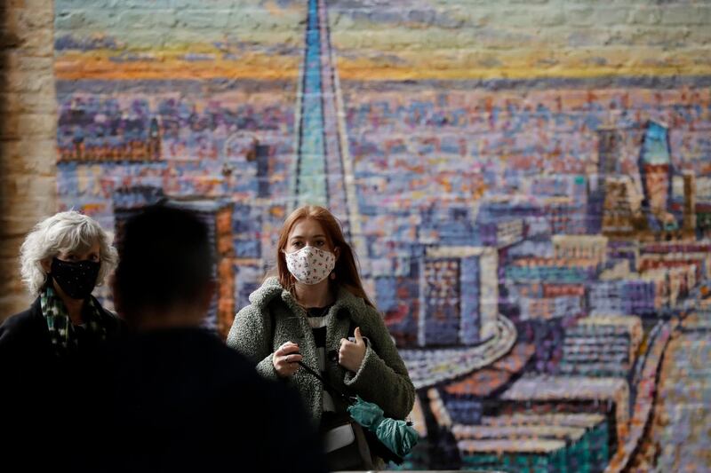 People wear face coverings as they walk past a recently painted mural entitled "London Cityscape" by Australian street artist James Cochran, in London. AP Photo