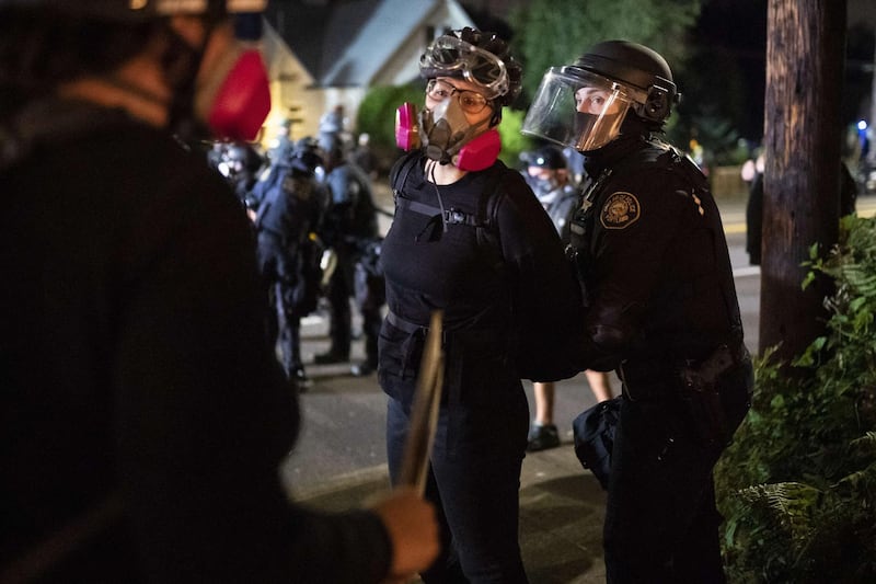 Two protesters carry on a  conversation while one is arrested by a Portland police officer in Portland, Oregon. AFP