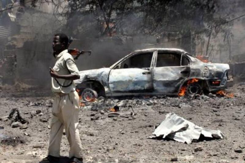 EDS NOTE: GRAPHIC CONTENT - A Somali soldier keeps guard near burned bodies and a burning vehicle at the scene of an explosion in Mogadishu, Somalia, Tuesday, Oct. 4, 2011. A rescue official says scores of people were killed after a car laden with explosives blew up in front of the Ministry of Education in the Somali capital of Mogadishu. (AP Photo/Mohamed Sheikh Nor) *** Local Caption ***  Somalia Explosion.JPEG-04955.jpg