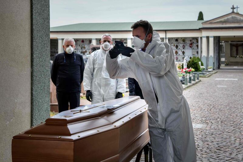 This picture taken on March 23, 2020 shows a pallbearer taking a picture of a coffin for the relatives of a deceased person at the cemetery of Grassobbio in the province of Bergamo, as they could not attend the ceremony because they are in quarantine as a result of the COVID-19 novel coronavirus.  / AFP / Piero CRUCIATTI
