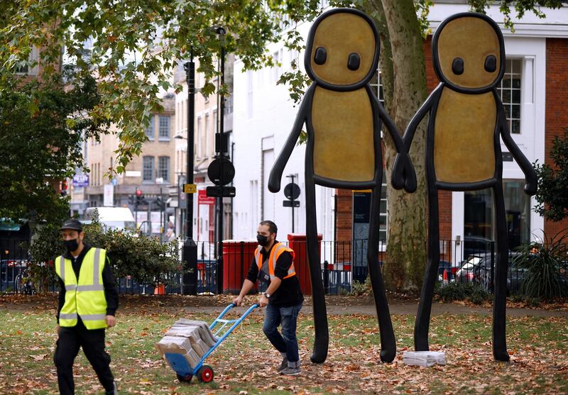 Staff working for British street artist STIK move bundles of local newspapers containing free copies of his artwork to be given away to local residents, during the unveiling of his bronze sculpture "Holding Hands" in Hoxton Square, London, Britain September 23, 2020. Picture taken September 23, 2020. REUTERS/John Sibley