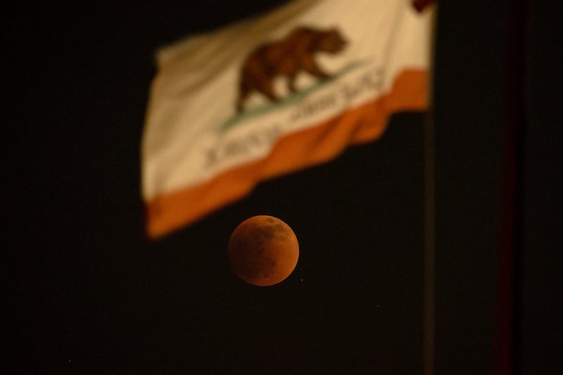 A total lunar eclipse is seen behind a California State flag, in El Monte. AP
