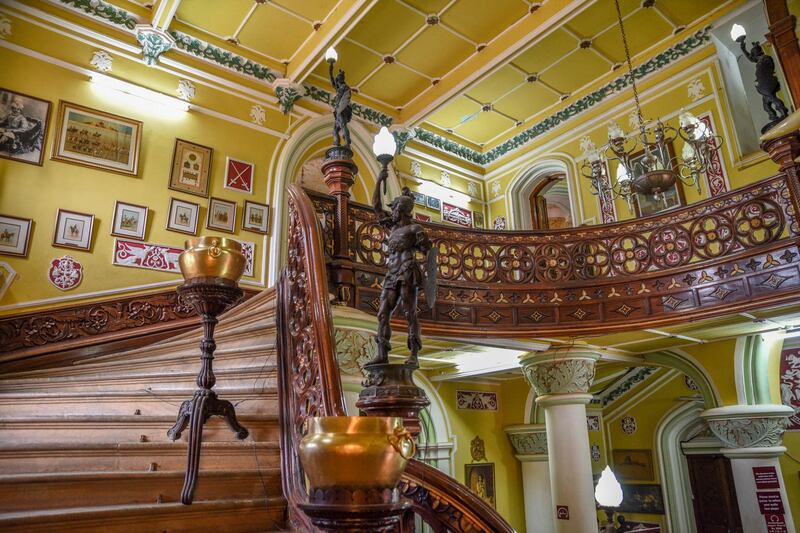 A grand staircase is embellished with complex woodwork featuring flowers, stars and royal crests, flanked by a lemon-yellow wall. Courtesy Ronan O'Connell