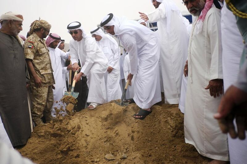 Sheikh Saif and Sheikh Hazza, holding shovels, are joined by Sheikh Mohammed bin Saqr at the grave of First Lt Al Shehi. Antonie Robertson/The National