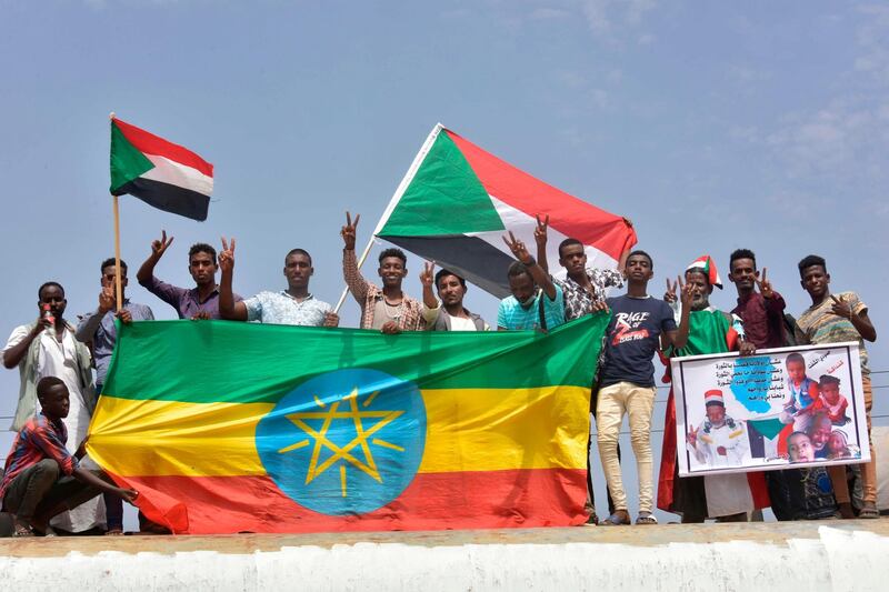 Men stand behind a large Ethiopian flag and wave flags of Sudan as protesters from the city of Atbara arrive at the Bahari station in Khartoum, to celebrate transition to civilian rule.   AFP