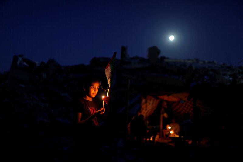 A Palestinian from Zawaraa family holds a candle near a makeshift tent amid the rubble of their houses, which were destroyed during Israeli air strikes on Gaza. Reuters