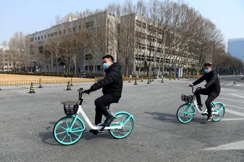 Two men wear face masks as a preventive measure against the COVID-19 coronavirus as they ride bikes in the empty grounds of Tsinghua University in Beijing on February 28, 2020. - The university, along with others in Beijing, has postponed the official start of the new semester due to the coronavirus outbreak, but has instead offered online courses. China reported 44 more deaths from the novel coronavirus epidemic on February 28 and 327 fresh cases, the lowest daily figure for new infections in more than a month. (Photo by GREG BAKER / AFP)