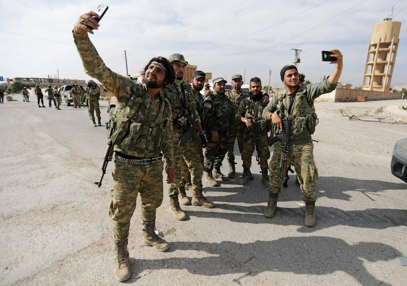 Turkey-backed Syrian rebel fighters take pictures with mobile phones at the border town of Tel Abyad, Syria. REUTERS