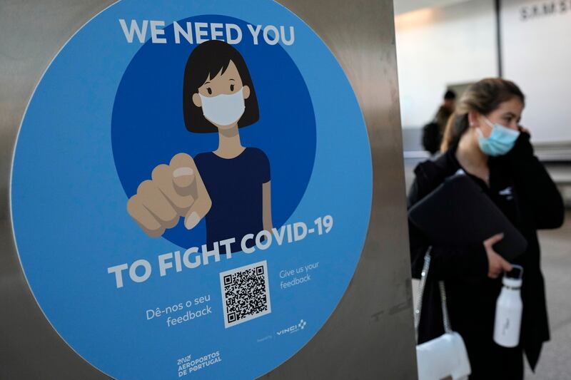 A woman wearing a face mask walks past a Covid-19 awareness sign at Lisbon's international airport.  Portugal is bringing back some tight pandemic restrictions, less than two months after scrapping most of them when the goal of vaccinating 86% of the population against Covid-19 was reached.  AP