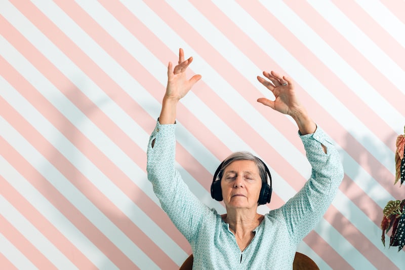 Elderly Lady In Her Seventies Listens To Music With Headphones Moving Her Arms In The Air. Getty Images