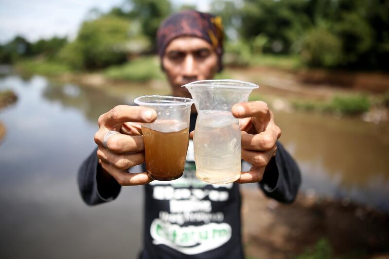 Environmental activist Deni Riswandani holds up cups of water from the Citarum river (R) and water from a tributary which runs through an area densely populated with textile factories (L) where the two meet near Majalaya, south-east of Bandung, West Java province, Indonesia, January 26, 2018. REUTERS/Darren Whiteside  SEARCH "WHITESIDE CITARUM" FOR THIS STORY. SEARCH "WIDER IMAGE" FOR ALL STORIES.     TPX IMAGES OF THE DAY
