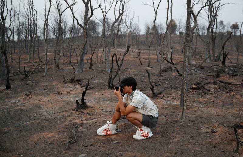 Jesus Alonzo-Manzo wears bags to keep his shoes clean while taking pictures of his cousin on a hillside burned in the Carr Fire, in Redding, California. John Locher/AP Photo