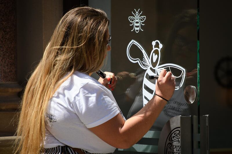 A woman paints the Manchester Bee icon onto a window on the first anniversary of the terrorist attack in central Manchester. Getty