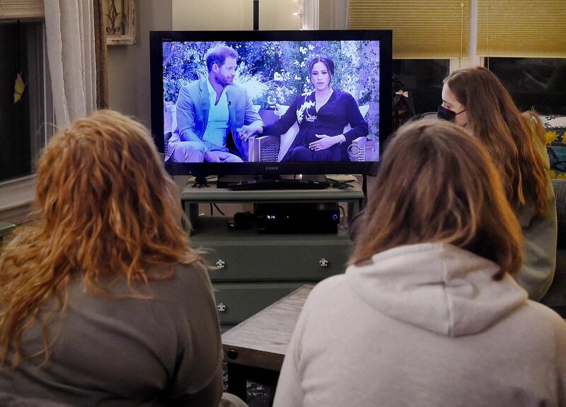 This photo illustration shows people wearing face masks, watch a televised conversation between Britain's Prince Harry with his wife Meghan Markle and US host Oprah Winfrey, in Arlington, Virginia March 7, 2021. Britain's royal family on Sunday braced for further revelations from Prince Harry and his American wife, Meghan, as a week of transatlantic claim and counter-claim reaches a climax with the broadcast of their interview with Oprah Winfrey. The two-hour interview with the US TV queen is the biggest royal tell-all since Harry's mother princess Diana detailed her crumbling marriage to his father Prince Charles in 1995.  / AFP / OLIVIER DOULIERY
