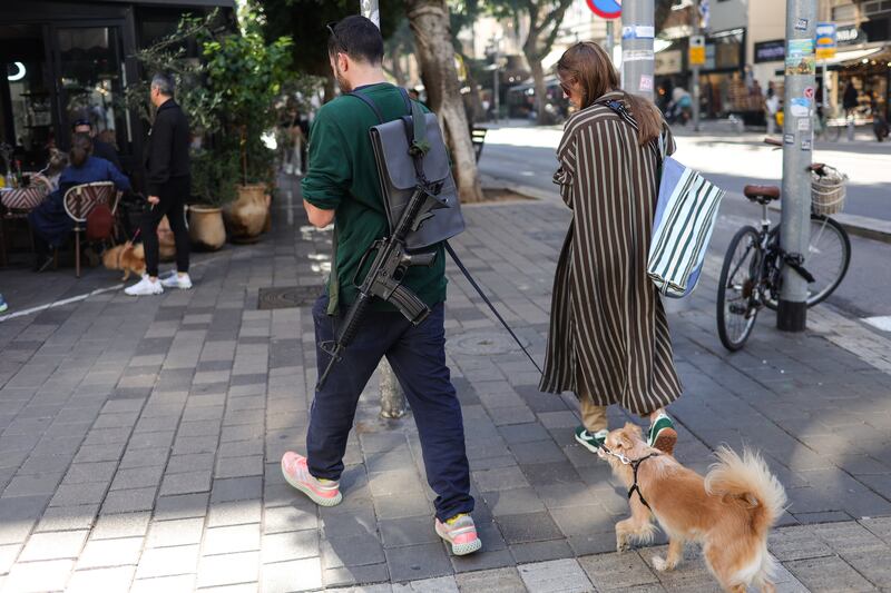 A man carries an assault rifle on Dizengoff Street, in Tel Aviv. The continuing war with Hamas raises political risk for Israel and weakens its institutions, Moody's says. EPA
