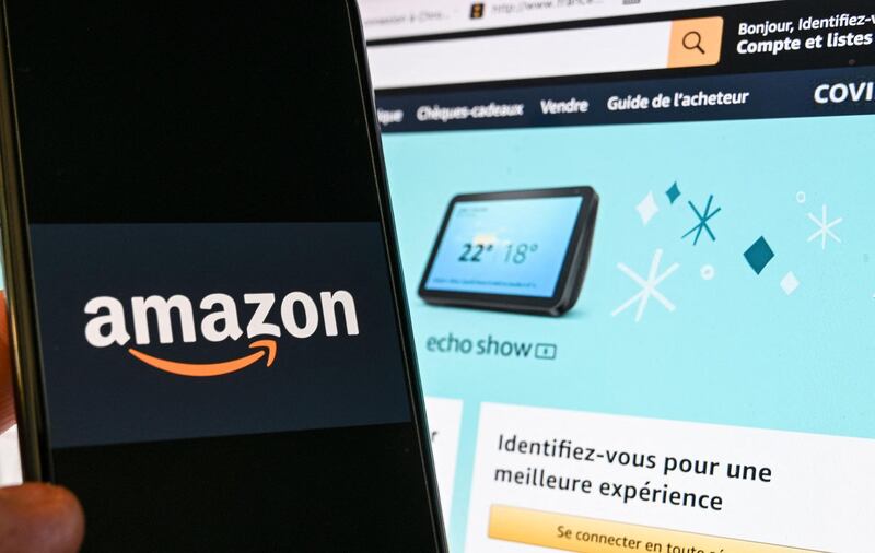 (FILES) In this file photograph taken on November 18, 2020 in Lille, a person poses with a smartphone showing an Amazon logo, in front of a computer screen displaying the home page of Amazon France sales website.  Amazon said on May 10, 2021 it blocked more than 10 billion suspected listings of counterfeit goods on its platform last year as part of a global crackdown in the face of pressure from consumers, brands and regulators. The e-commerce colossus made the announcement in its first "brand protection report," as part of its initiative to weed out listings of fakes by third-party sellers.
 / AFP / DENIS CHARLET
