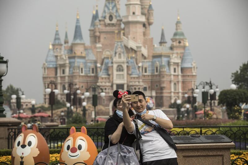 Visitors with protective masks pose for photographs in front of the Enchanted Storybook at Shanghai Disneyland. Bloomberg