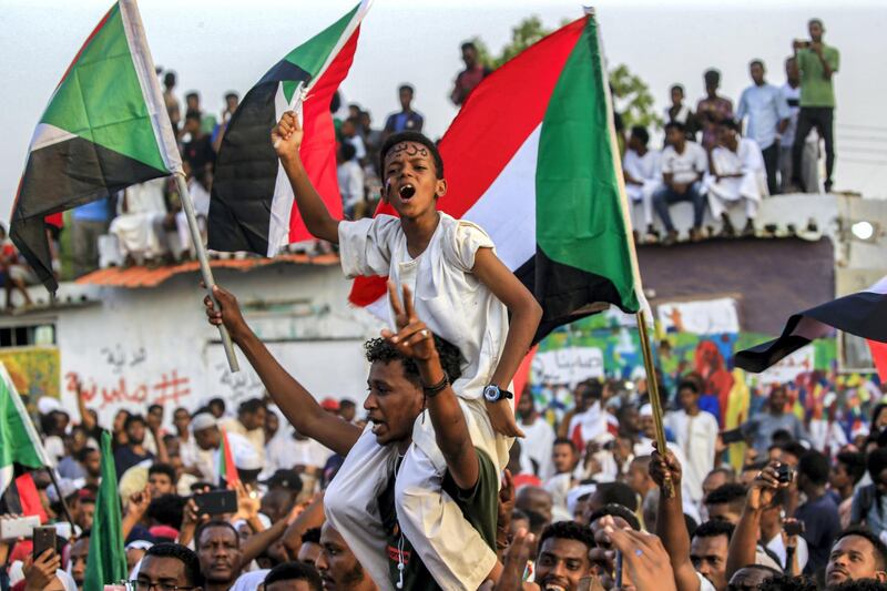 A Sudanese boy wearing facepaint on his forehead reading in Arabic "civilian" chants slogans while seated on the shoulders of a man as people celebrate after protest leaders struck a deal with the ruling generals on a new governing body, in the capital Khartoum's eastern district of Burri on July 5, 2019, - The deal, reached in the early hours of July 5 after two days of hard-won talks brokered by Ethiopian and African Union mediators, provides for the interim governing body to have a rotating presidency, as a compromise between the positions of the generals and the protesters. The blueprint proposes that a general hold the presidency for the first 18 months of a three-year transition, with a civilian taking over for the rest. (Photo by ASHRAF SHAZLY / AFP)