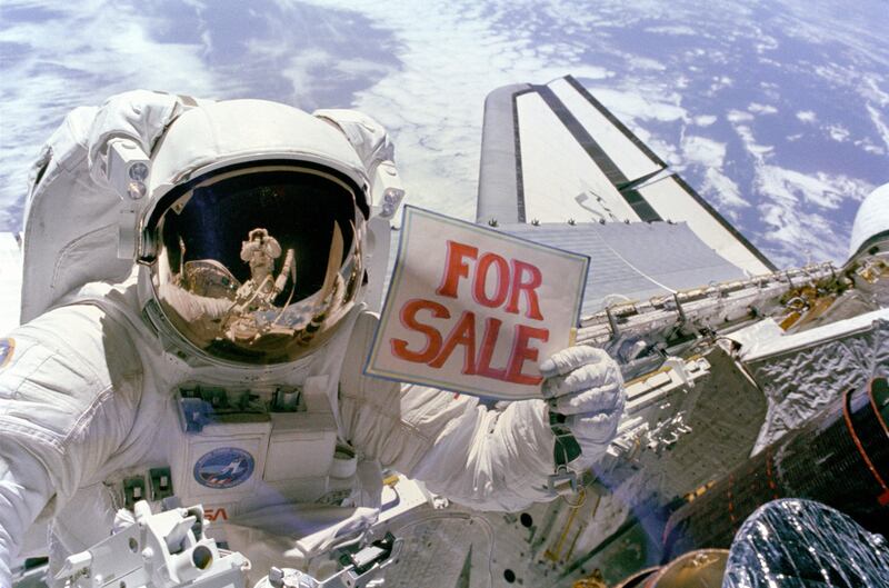 Astronaut Dale A. Gardner, having just completed the major portion of his second extravehicular activity (EVA) period in three days, holds up a "For Sale" sign refering to the two satellites, Palapa B-2 and Westar 6 that they retrieved from orbit after their Payload Assist Modules (PAM) failed to fire. Astronaut Joseph P. Allen IV, who also participated in the two EVAs, is reflected in Gardner's helmet visor. A portion of each of two recovered satellites is in the lower right corner, with Westar 6 nearer Discovery's aft. 