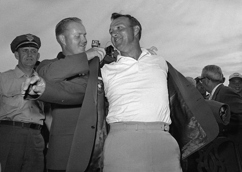 In this April 12, 1964 file photo, Arnold Palmer, right, slips into his green jacket with help from Jack Nicklaus after winning the Masters golf championship, in Augusta, Georgia. AP Photo