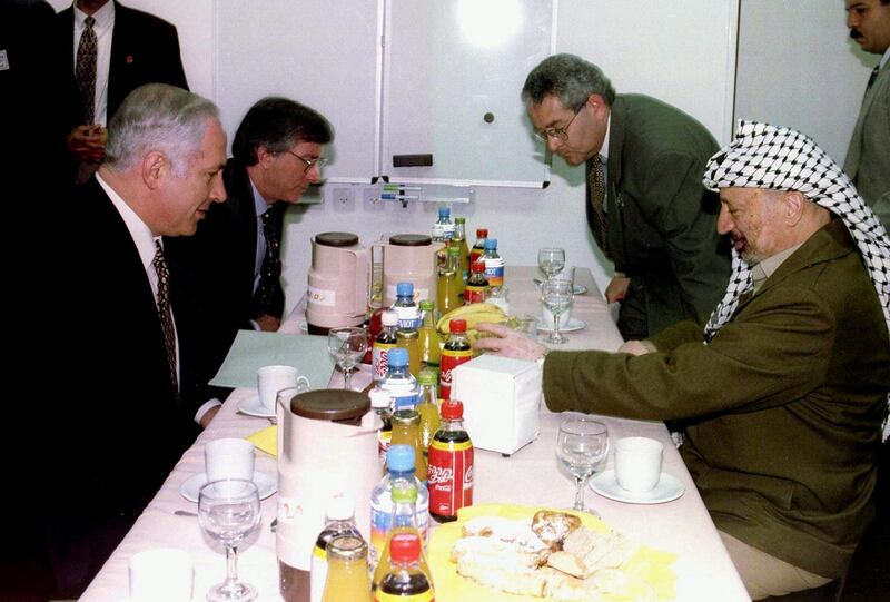 Israeli Prime Minister Benjamin Netanyahu (L) and Palestinian President Yasser Arafat (R) during their meeting at Erez Crossing point, northen Gaza Strip, December 24. Arafat and Netanyahu met here in search of an agreement to end Israeli occupation of Hebron and revive the peace process. In the background at left is U.S. mediator Dennis Ross.