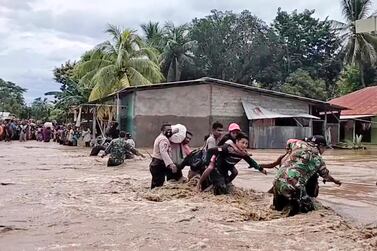 An image taken from video shows soldiers and police officers helping residents to cross a flooded road in Malaka Tengah, East Nusa Tenggara province, Indonesia, on April 5, 2021. AP Photo