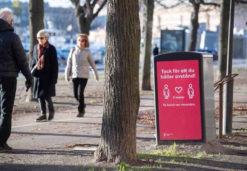 People strollIing in the cold but sunny weather pass a sign asking to maintain social distancing in Stockholm. EPA