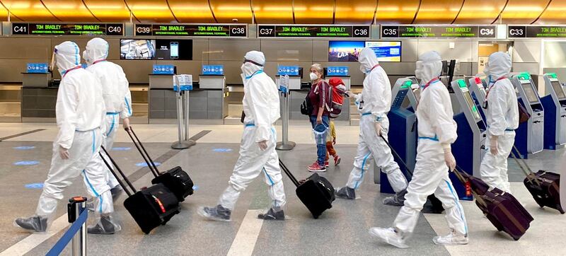 A woman, accompanied by a child, looks over as an airline crew wearing full personal protective equipment against COVID-19 walks through the international terminal at Los Angeles International Airport in Los Angeles. AP Photo
