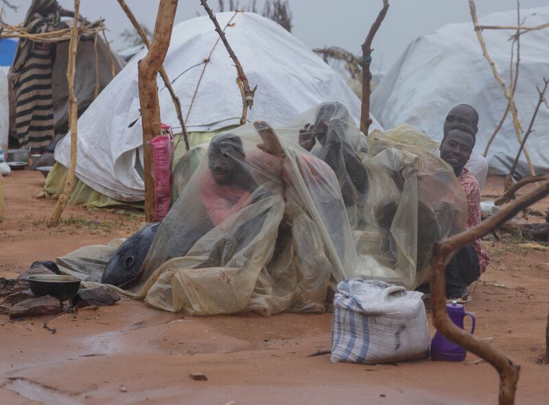 Sudanese refugees use plastic sheeting to shield themselves from the rain at the camp in Ourang, Chad.