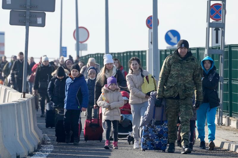 A Polish border guard assists refugees from Ukraine as they arrive to Poland at the Korczowa border crossing, Poland. AP Photo