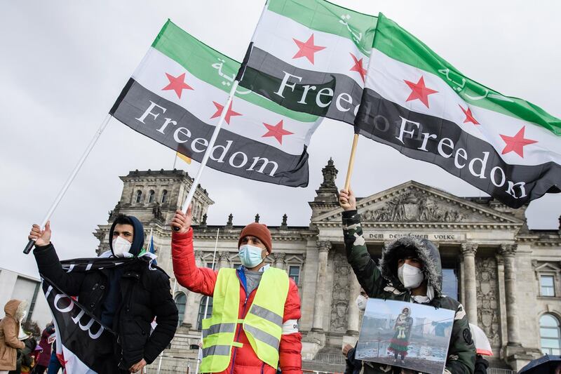 epa09073902 Participants of a rally on the occasion of the tenth anniversary of the Syrian Uprising hold Syrian flags reading the word 'freedom' in front of the Reichstag building, the seat of the German parliament, in Berlin, Germany, 14 March 2021. Syrians and their supporters commemorated missing, abducted and imprisoned persons and protested against the ongoing dictatorship in Syria, ten years after the civil unrest of the Syrian people starting from 15 March 2011.  EPA/CLEMENS BILAN