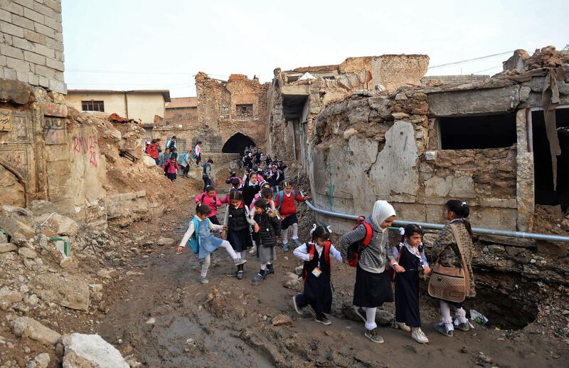 Iraqi students walk through a damaged road on their way back from school in the northern city of Mosul. AFP