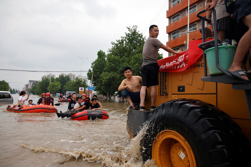 People riding boats and front loader make their way through a flooded road following heavy rainfall in Zhengzhou, Henan province, China.