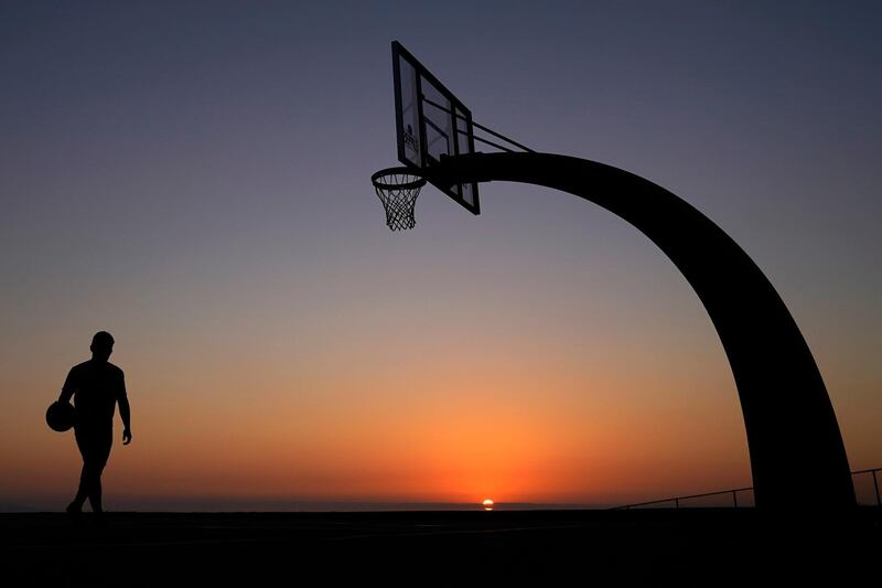 A Los Angeles resident plays on a basketball court at Angels Gate Park as the sun sets. AP