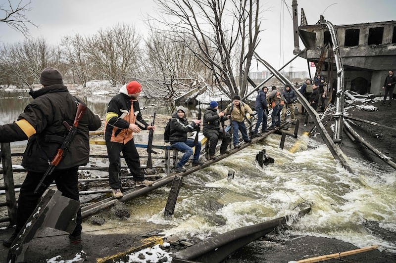 Members of an Ukrainian civil defence unit pass new assault rifles to the opposite side of a blown-up bridge on Kiev’s northern front. AFP